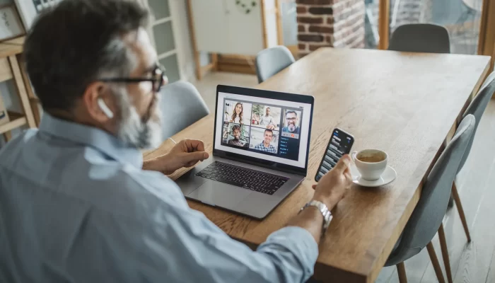 Image of man on in front of his laptop on a video call, whilst looking at his mobile phone.