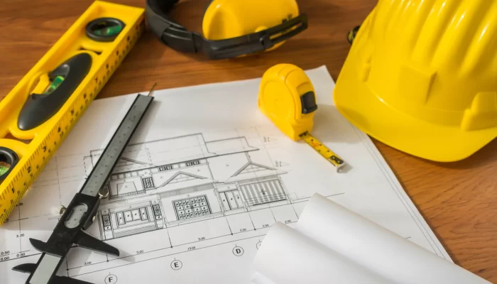 Image of blueprints, hard hat, leveler, measuring tape and construction headphones.