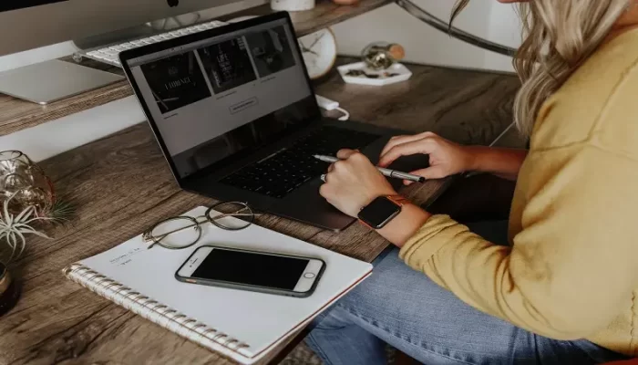 an image of someone working at their desk, with a laptop, notepad and iPhone.